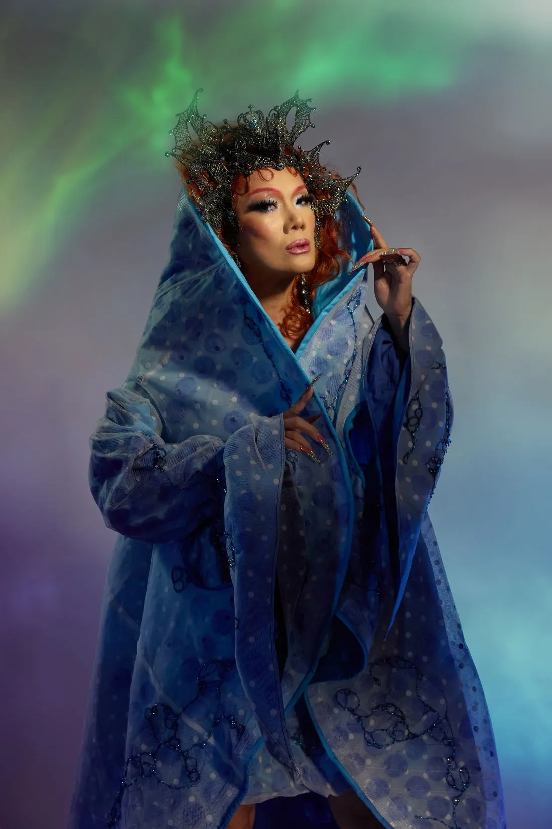 A Heals queen wrapped in a vast blue cloak under a crown of black lace